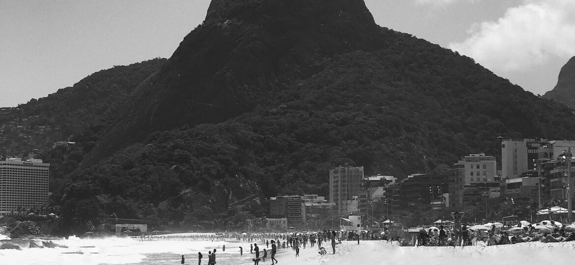 A black and white photo of a child running from the ocean on the sand with the dark silhouette of a hill in the background